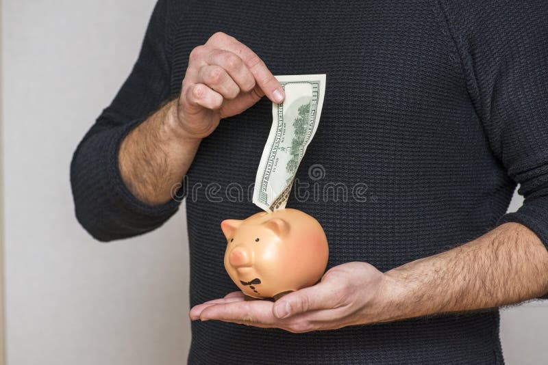 M?o masculina que p?e a nota de d?lar em um mealheiro Mão que põe o dólar da cédula do dinheiro em leitão para o dinheiro de salv imagem de stock royalty free M?o masculina que p?e a nota de d?lar em um mealheiro Mão que põe o dólar da cédula do dinheiro em leitão para o dinheiro de salv imagem de stock royalty free