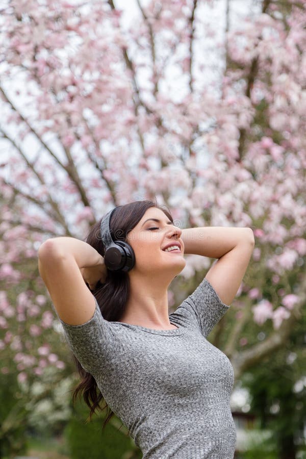 M?oda kobieta s?ucha muzyka na bezprzewodowych he?mofonach w parku z czere?niowego okwitni?cia drzewami fotografia stock M?oda kobieta s?ucha muzyka na bezprzewodowych he?mofonach w parku z czere?niowego okwitni?cia drzewami fotografia stock
