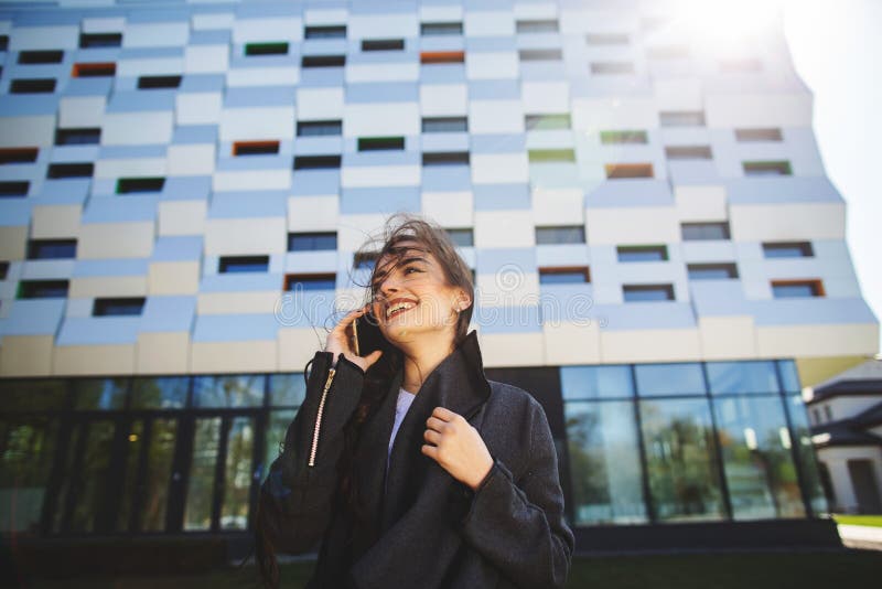 M?ody bizneswomanu m?wienie na telefonie kom?rkowym podczas plenerowej kawowej przerwy blisko budynku biurowego, czarny komunikac fotografia stock M?ody bizneswomanu m?wienie na telefonie kom?rkowym podczas plenerowej kawowej przerwy blisko budynku biurowego, czarny komunikac fotografia stock