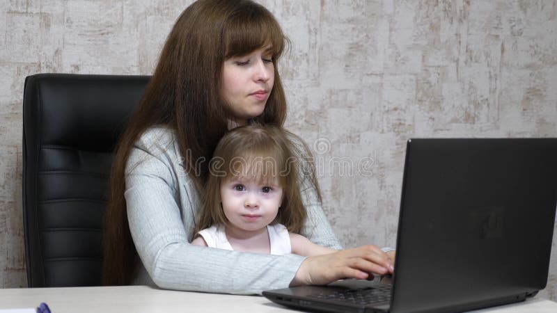 M?re de fonctionnement avec sa petite fille ? la table Femme occup?e travaillant sur l'ordinateur portable avec le b?b? sur des m images libres de droits M?re de fonctionnement avec sa petite fille ? la table Femme occup?e travaillant sur l'ordinateur portable avec le b?b? sur des m images libres de droits