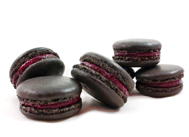 Macarons franceses pretos com escuro - enchimento vermelho do fruto isolado no fundo branco foto de stock Macarons franceses pretos com escuro - enchimento vermelho do fruto isolado no fundo branco foto de stock