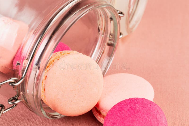 Macarons o macarrones franceses rosados, cayendo de un tarro de cristal sobre un fondo rosado del mantel, primer fotografía de archivo libre de regalías Macarons o macarrones franceses rosados, cayendo de un tarro de cristal sobre un fondo rosado del mantel, primer fotografía de archivo libre de regalías