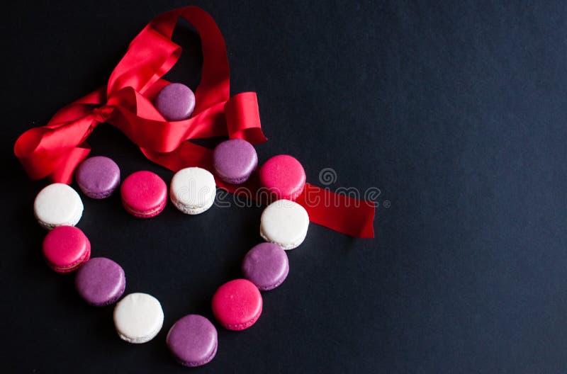 Macaroon laid out on a black background in the form of a heart with red ribbon. colorful almond cookies, pastel colors. Present stock photography Macaroon laid out on a black background in the form of a heart with red ribbon. colorful almond cookies, pastel colors. Present stock photography