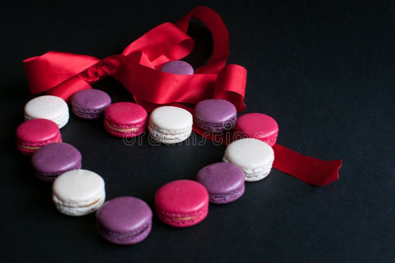 Macaroon laid out on a black background in the form of a heart with red ribbon. colorful almond cookies, pastel colors. Present stock photos Macaroon laid out on a black background in the form of a heart with red ribbon. colorful almond cookies, pastel colors. Present stock photos