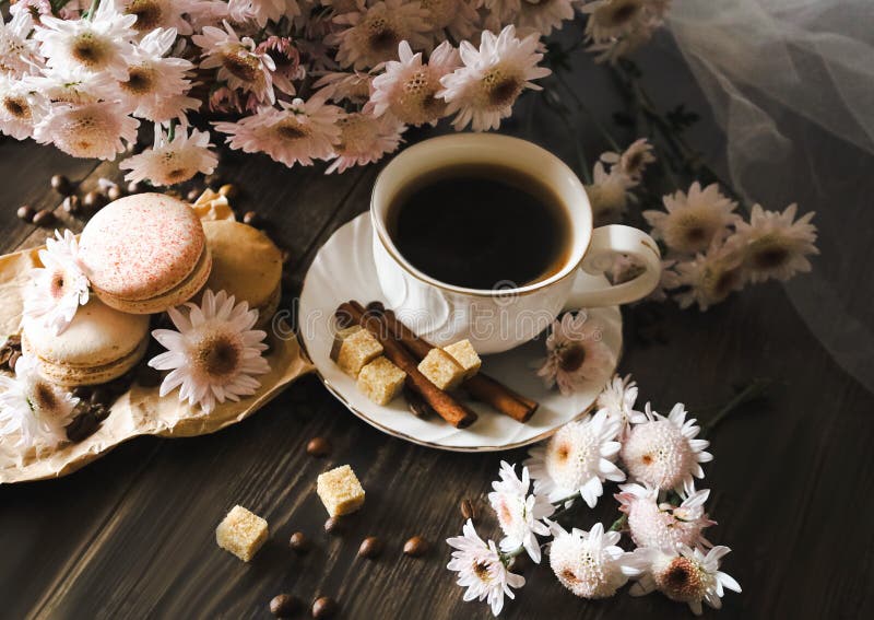 Macaroons, pink chrysanthemums and a white cup of coffee. Still life on a dark background.