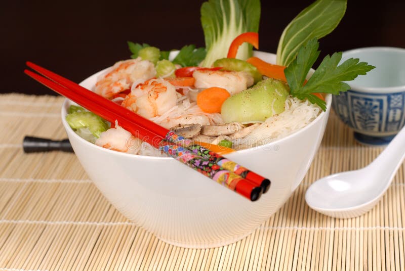 A bowl of udon noodles with vegetables and seafood with chopsticks. A bowl of udon noodles with vegetables and seafood with chopsticks