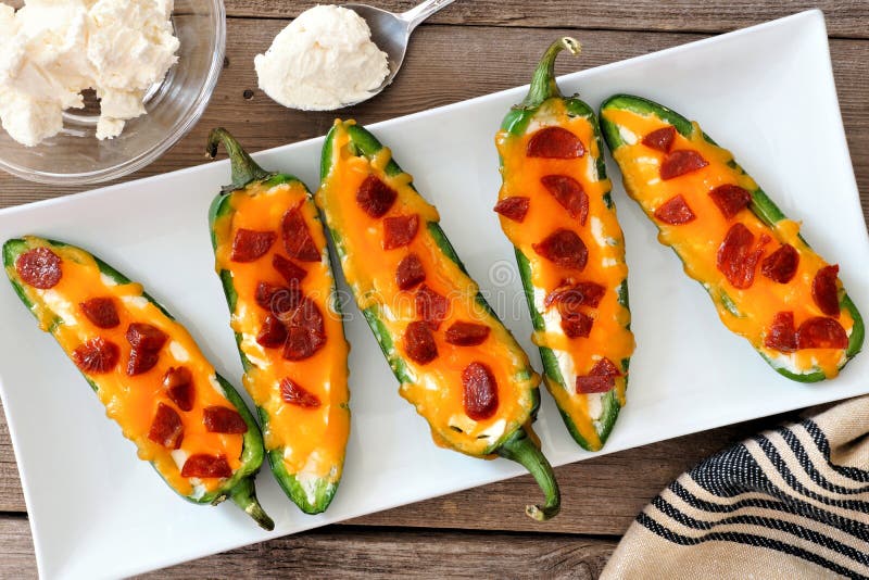 Group of jalapeno poppers with cheese and pepperoni on a white serving plate, overhead scene. Group of jalapeno poppers with cheese and pepperoni on a white serving plate, overhead scene