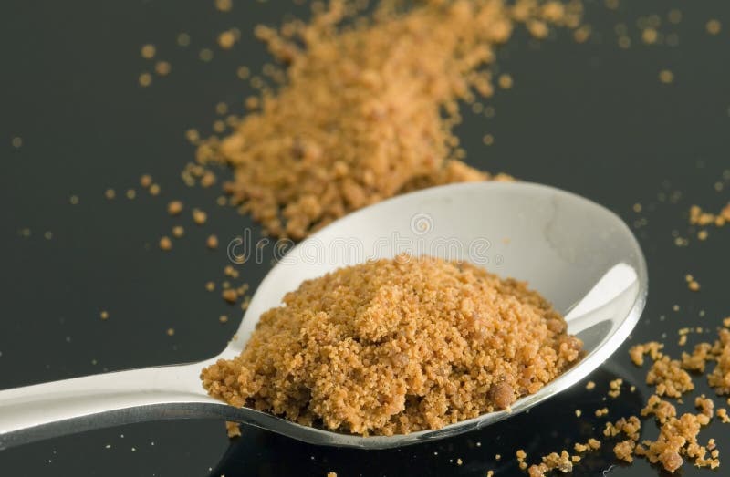 Close-up of ground red orange color or colour of mace the ground outer cover of the nutmeg plant used as a spice sitting on a silver spoon on a black plate and show the texture of the ground orange powder it is from the latin macir. Close-up of ground red orange color or colour of mace the ground outer cover of the nutmeg plant used as a spice sitting on a silver spoon on a black plate and show the texture of the ground orange powder it is from the latin macir