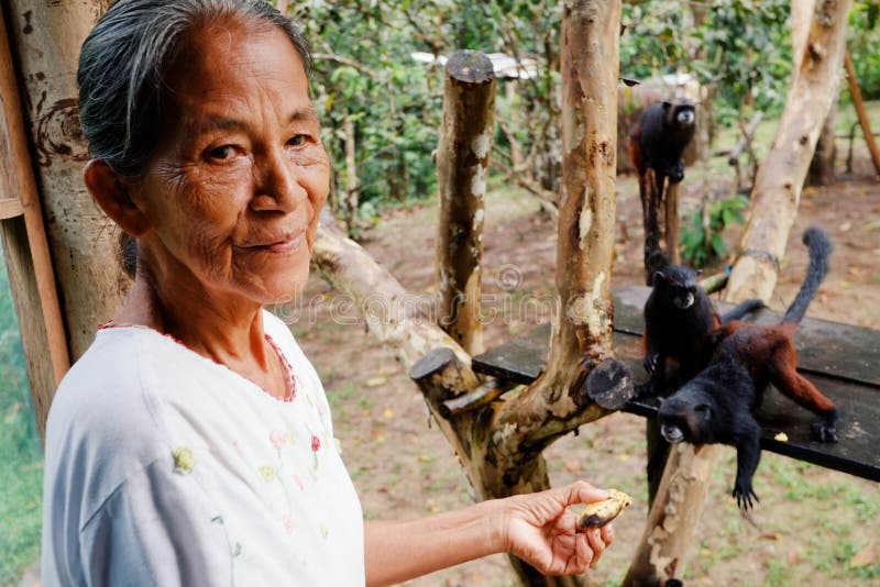 Macedonia, Amazonia / Colombia - MAR 15 2016: local ticuna tribe member lady feeding pet monkeys with bananas in the rainforest jungle village. Macedonia, Amazonia / Colombia - MAR 15 2016: local ticuna tribe member lady feeding pet monkeys with bananas in the rainforest jungle village