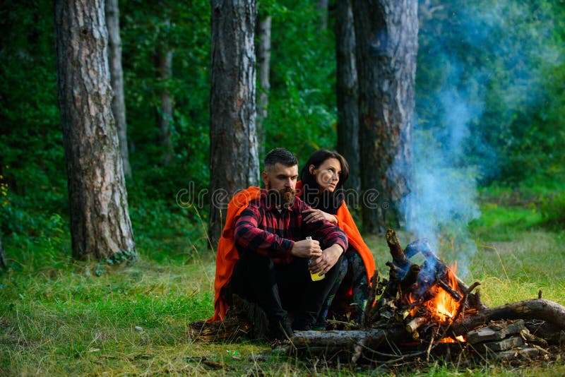 Macho avec de la bière se reposant près du feu, appréciant des vacances avec l'épouse photographie stock libre de droits Macho avec de la bière se reposant près du feu, appréciant des vacances avec l'épouse photographie stock libre de droits