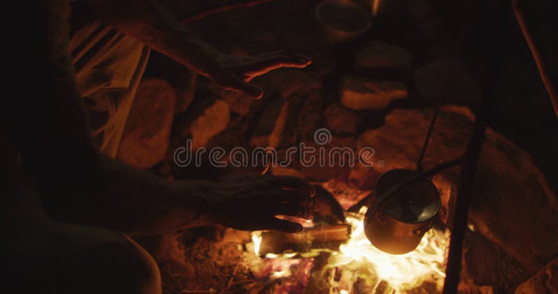 Macho caucásico sobreviviente calentando las manos en una fogata nocturna en el campamento en el desierto