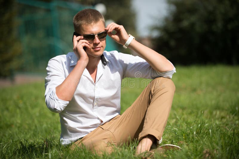 Macho considerável aprecia o dia de verão Homem de negócios nos óculos de sol em exterior ensolarado O homem relaxa na grama verd fotos de stock Macho considerável aprecia o dia de verão Homem de negócios nos óculos de sol em exterior ensolarado O homem relaxa na grama verd fotos de stock
