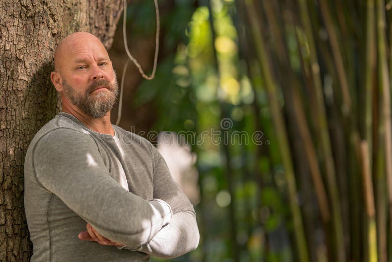 Macho man with arms crossed leaning on a tree