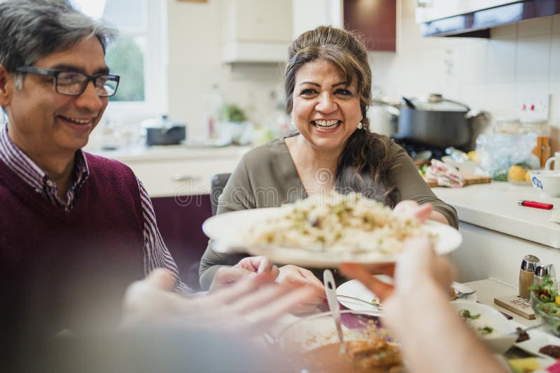 Point of view shot of a mature mother passing a serving of curry and rice to her son at the dining table. Point of view shot of a mature mother passing a serving of curry and rice to her son at the dining table.