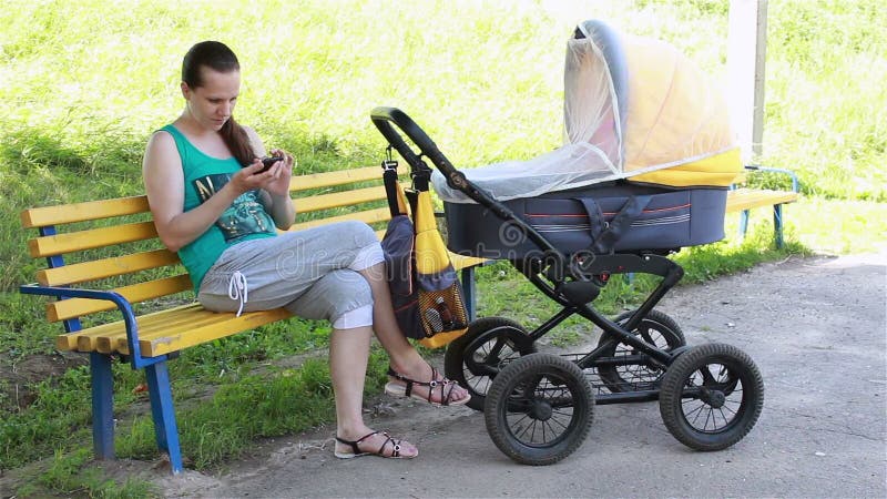 Macierzysty obsiadanie w parku stacza się spacerowicza i patrzeć smartphone