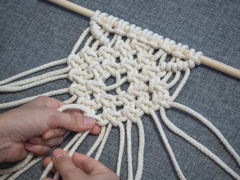 Macrame. Girl weaves macrame. White thread, female hand, grey background, close-up