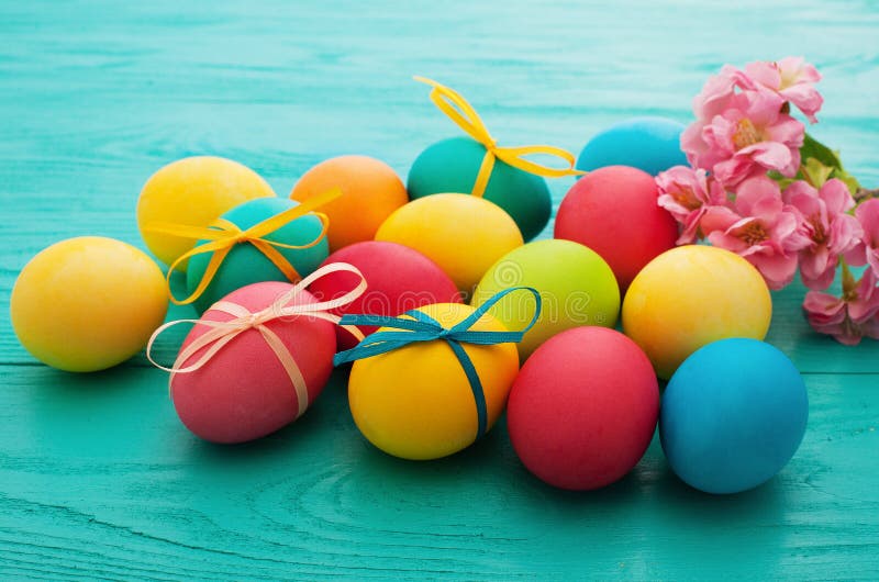 Macro Colorful Easter eggs on blue wooden kitchen table and pink flowers. Egg background. Selective focus stock images