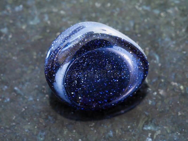 macro shooting of mineral rock specimen - polished blue goldstone gemstone on dark granite background