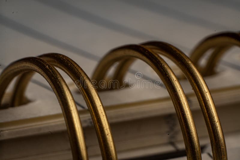 Close-up of spiral binding showcasing intricate details in an office notebook. A macro view captures the shiny metal rings of a spiral binding within an empty notebook. The lined pages await notes or reminders, emphasizing workspace organization.