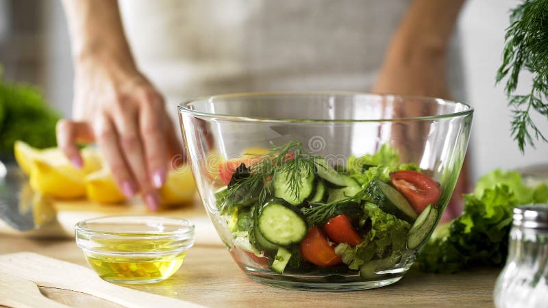Madame tenant le morceau de citron et l'huile d'olive pour s'habiller, saladier organique sur la table photographie stock Madame tenant le morceau de citron et l'huile d'olive pour s'habiller, saladier organique sur la table photographie stock