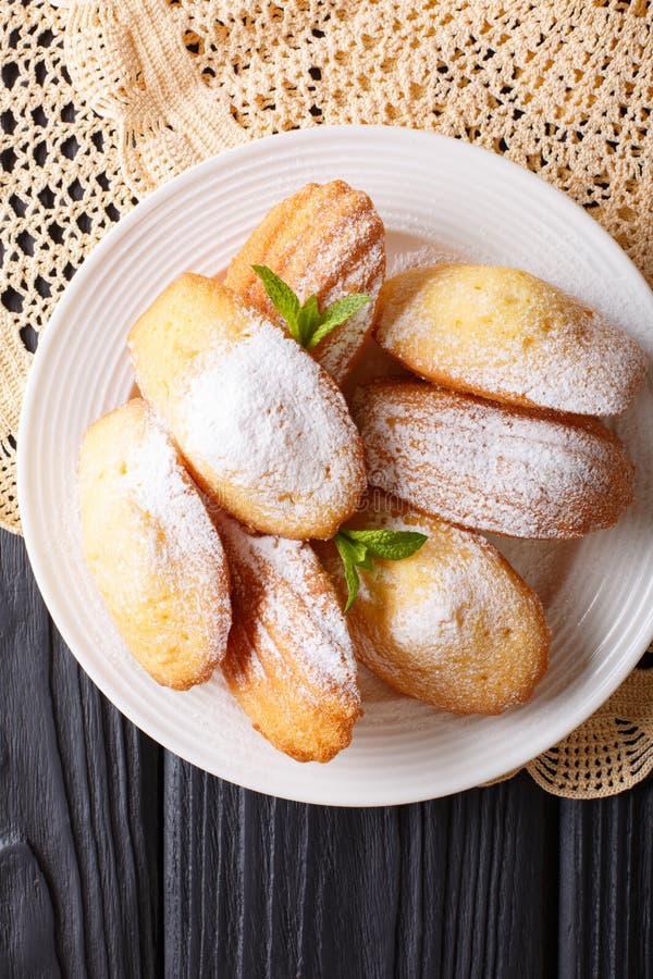 Madeleine biscuits with powdered sugar and mint closeup on a plate on the table. vertical top view.