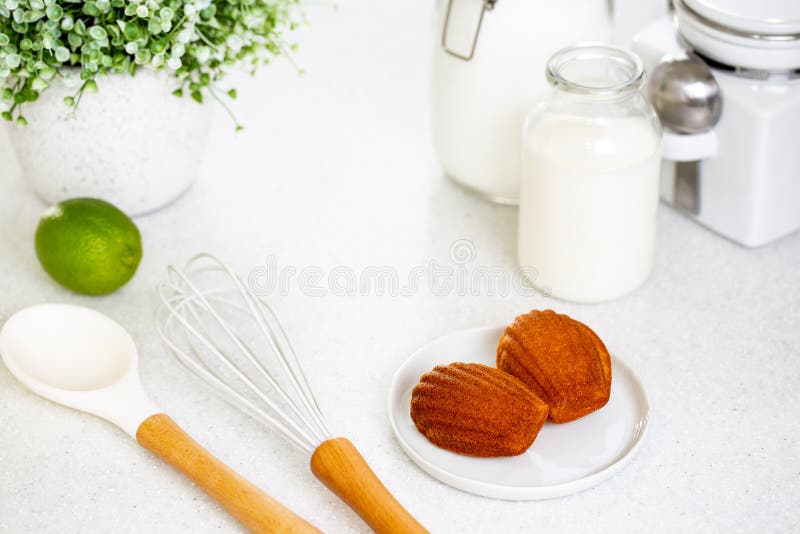 Madeleine cookie or French sponge cake in a white plate alongside white kitchen utensils, lime, sugar, milk and flour j stock image Madeleine cookie or French sponge cake in a white plate alongside white kitchen utensils, lime, sugar, milk and flour j stock image