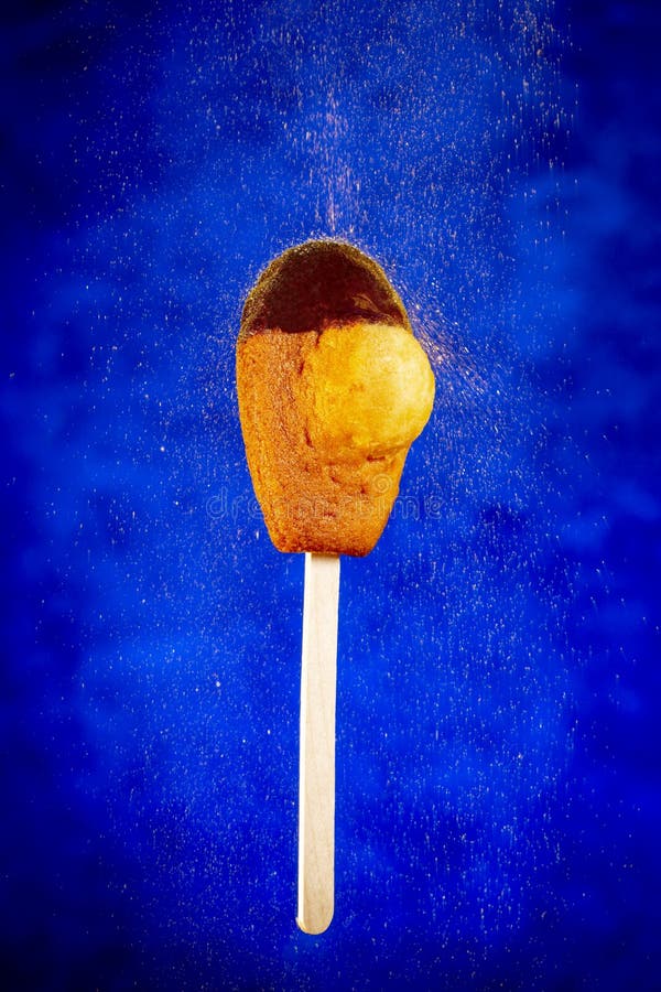 Madeleine cookie or French sponge on an ice cream stick with a gold particules shower over a blue background stock photography Madeleine cookie or French sponge on an ice cream stick with a gold particules shower over a blue background stock photography