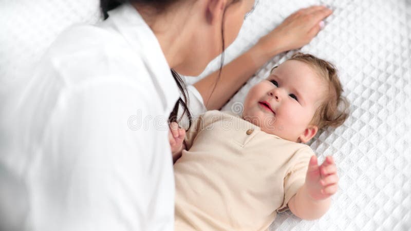 Madera nutritiva con camisa blanca uniéndose con un niño sonriente con traje corporal beige apoyándose en una manta blanda almacen de video