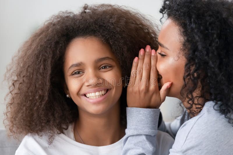 Madre afroamericana che bisbiglia all'orecchio teenager sorridente della figlia