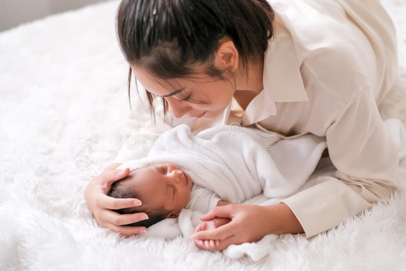 Madre asiática toca la cabeza de su bebé recién nacido con emoción de cuidado y amor en cama blanca imagenes de archivo Madre asiática toca la cabeza de su bebé recién nacido con emoción de cuidado y amor en cama blanca imagenes de archivo