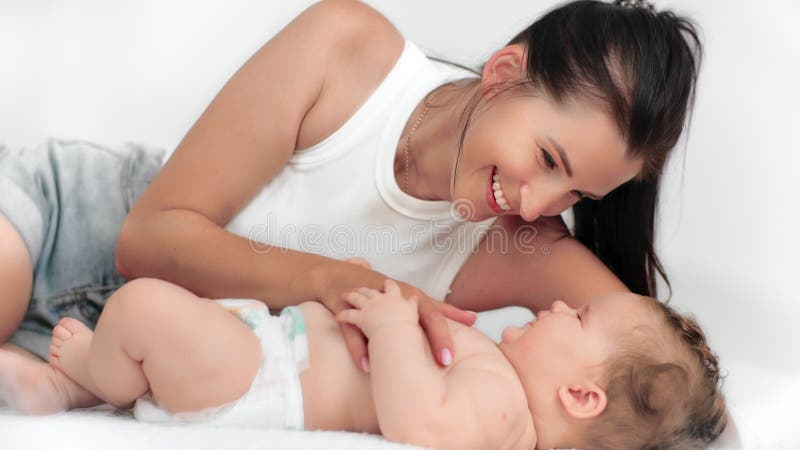 Madre blanca anidada junto a un recién nacido que hace cosquillas suaves en un fondo blanco limpio que irradia íntima madre almacen de metraje de vídeo