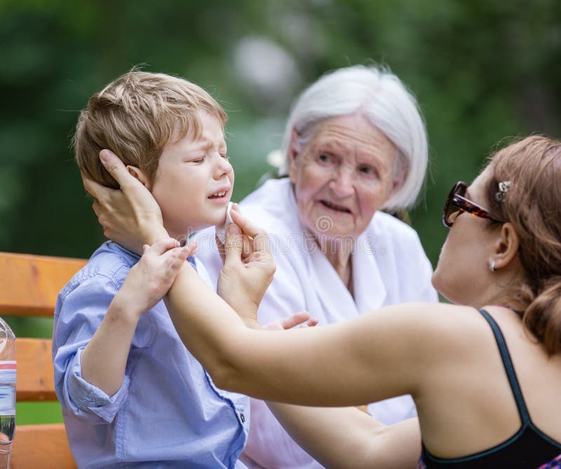 Madre che tratta raschiatura sul mento del ` s del figlio fotografia stock Madre che tratta raschiatura sul mento del ` s del figlio fotografia stock