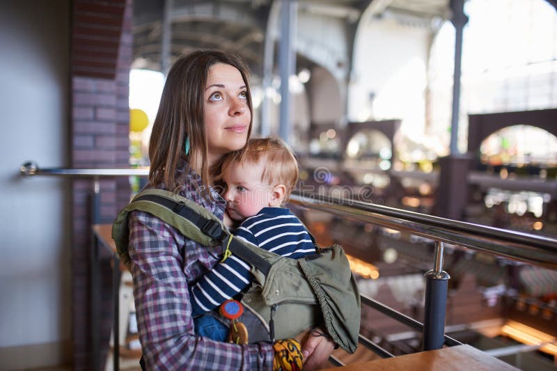 Madre con il bambino di trasporto ergobaby in caff? immagini stock libere da diritti Madre con il bambino di trasporto ergobaby in caff? immagini stock libere da diritti