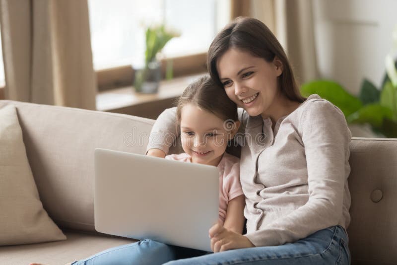 Madre con la figlia che si siede sul film di sorveglianza dello strato sul computer portatile immagine stock libera da diritti Madre con la figlia che si siede sul film di sorveglianza dello strato sul computer portatile immagine stock libera da diritti