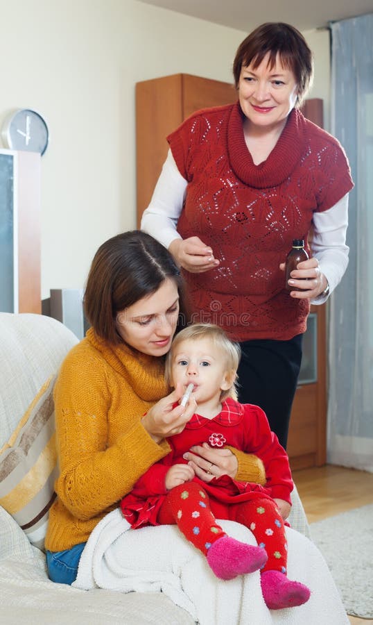 Madre con la nonna matura che dà medicinale al bab indisposto immagine stock libera da diritti Madre con la nonna matura che dà medicinale al bab indisposto immagine stock libera da diritti