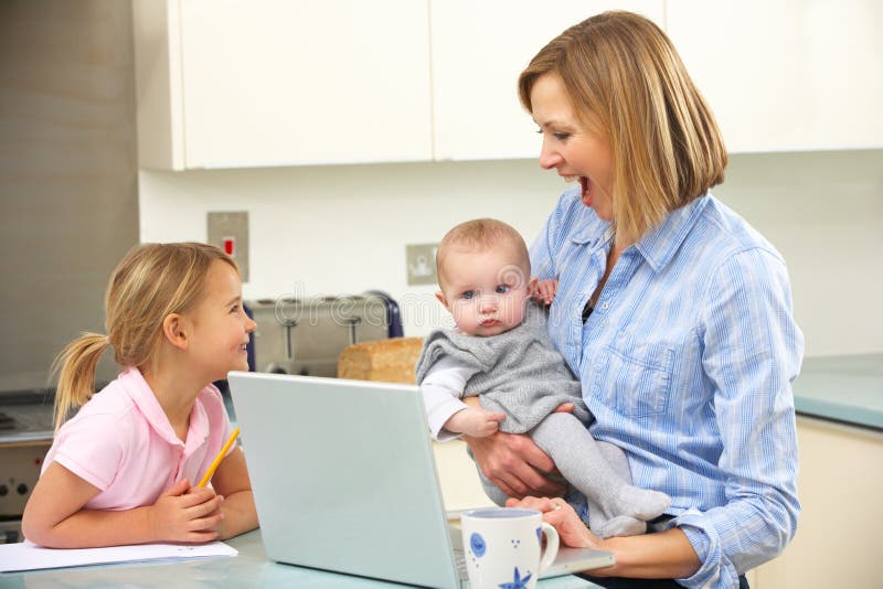 Madre con los niños que usan la computadora portátil en cocina imagen de archivo Madre con los niños que usan la computadora portátil en cocina imagen de archivo