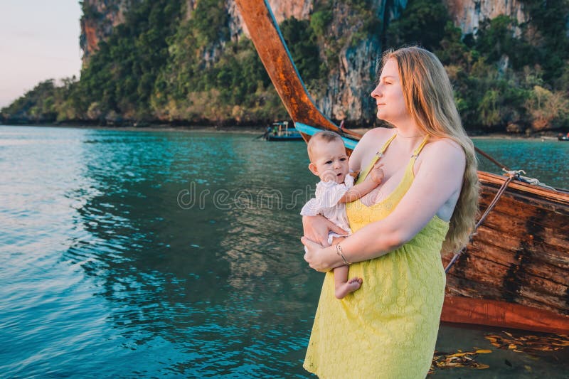 Madre con un bebé disgustado parada en el muelle contra el fondo del agua en la madrugada y encontrarse con el amanecer en