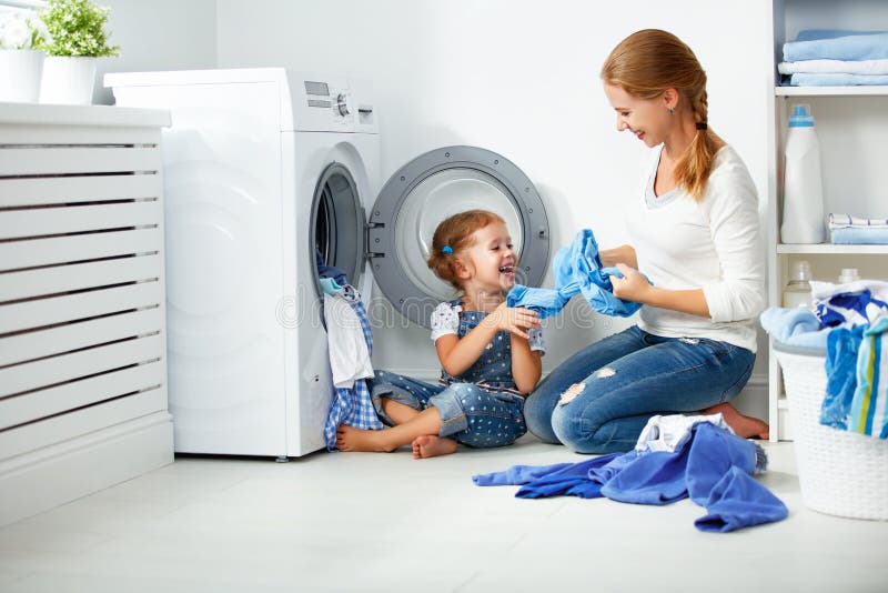 Madre della famiglia ed assistente della ragazza del bambino piccolo nella stanza di lavanderia vicino alla lavatrice immagine stock
