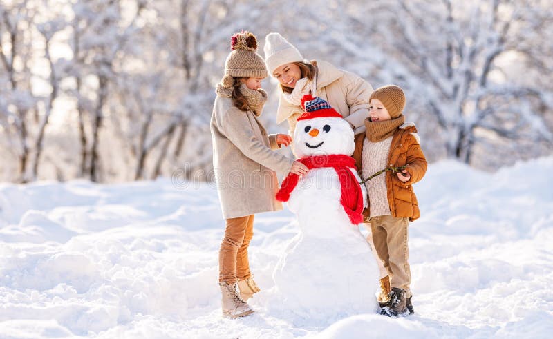 Madre di famiglia felice e due bambini piccoli fanno un pupazzo di neve insieme all'aperto nel parco invernale