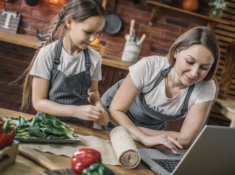 Madre e figlia al computer portatile sulla cucina fotografia stock Madre e figlia al computer portatile sulla cucina fotografia stock