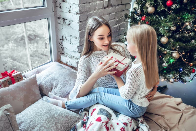 Madre e figlia felici con il contenitore di regalo sopra stanza con il fondo dell'albero di Natale fotografia stock Madre e figlia felici con il contenitore di regalo sopra stanza con il fondo dell'albero di Natale fotografia stock