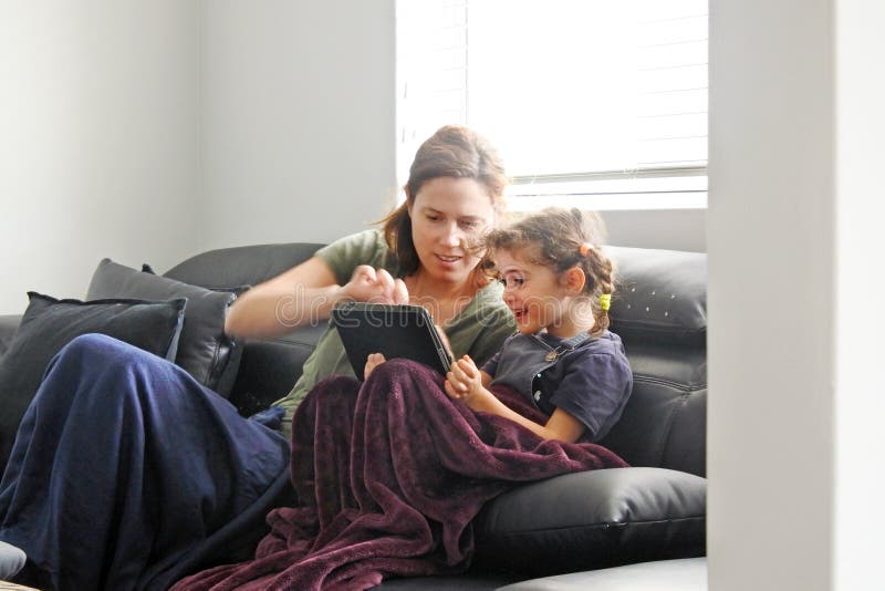 Mother and daughter using a tablet in living room while forced to stay at home because government policies efforts to prevent pandemic coronavirus COVID-19 spreading. Real people. Copy space. Mother and daughter using a tablet in living room while forced to stay at home because government policies efforts to prevent pandemic coronavirus COVID-19 spreading. Real people. Copy space