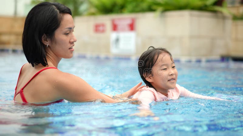 Madre e hija china asiática aprendiendo a nadar en la piscina almacen de metraje de vídeo