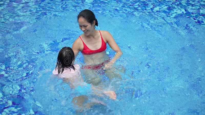 Madre e hija china asiática en cámara lenta jugando en la piscina metrajes