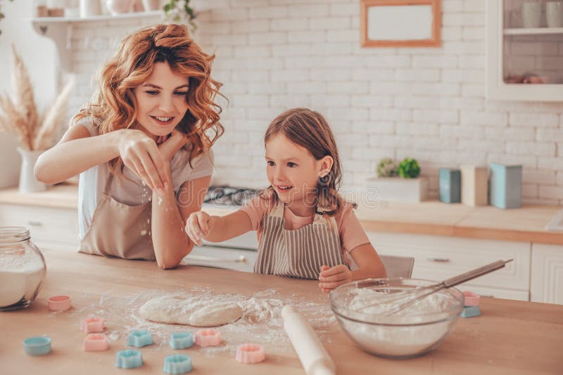 Madre e hija pequeña espolvoreando harina sobre la masa para galletas fotos de archivo libres de regalías