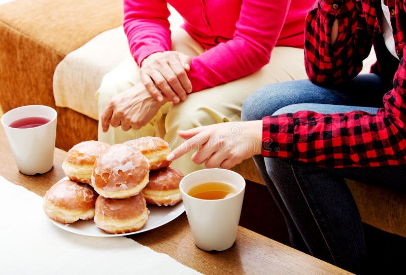 Madre e hija que se sientan en el sofá con los anillos de espuma y el té en la tabla imagen de archivo Madre e hija que se sientan en el sofá con los anillos de espuma y el té en la tabla imagen de archivo