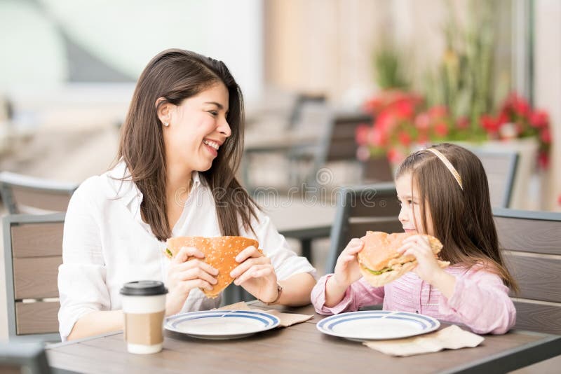 Madre e hija sonrientes que comen una hamburguesa imagen de archivo libre de regalías Madre e hija sonrientes que comen una hamburguesa imagen de archivo libre de regalías