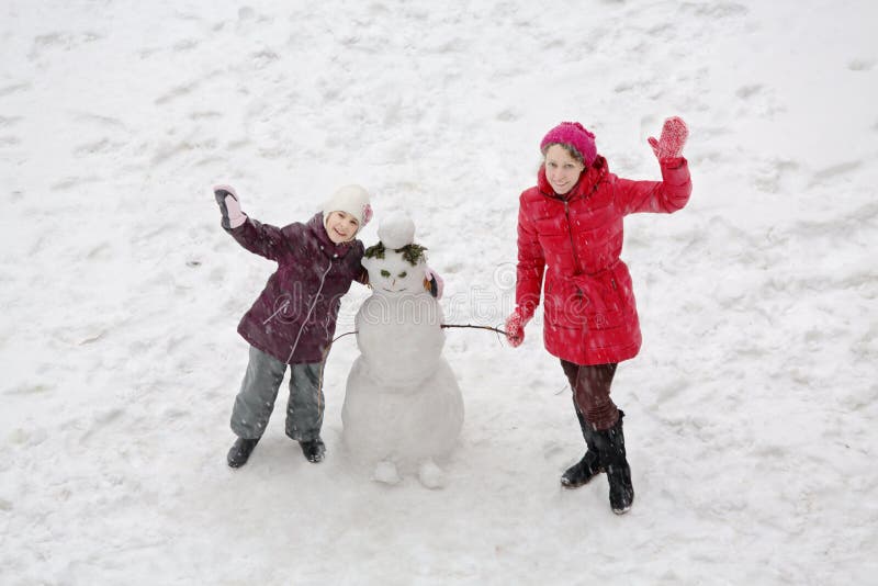 Madre e hija sonrientes que se colocan al lado de un muñeco de nieve imagenes de archivo Madre e hija sonrientes que se colocan al lado de un muñeco de nieve imagenes de archivo