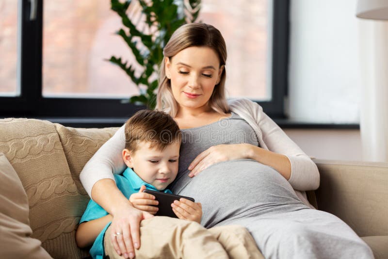 Madre E Hijo Embarazadas Con Smartphone En Casa Foto De Archiv