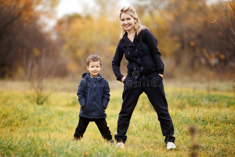 Madre e hijo jovenes en el otoño Forest Park, follaje amarillo ropa de sport Niño que lleva la chaqueta azul Familia incompleta imagenes de archivo Madre e hijo jovenes en el otoño Forest Park, follaje amarillo ropa de sport Niño que lleva la chaqueta azul Familia incompleta imagenes de archivo